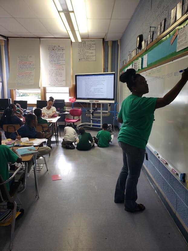 Teacher writing on whiteboard with students sitting in class Teacher writing on whiteboard with students sitting in class